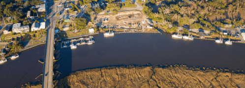 Aerial view of a river with boats, a construction site, and lush greenery along the shoreline.
