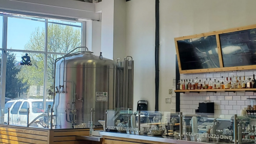 A modern café interior featuring a large brewing tank, a bar area, and large windows with natural light.