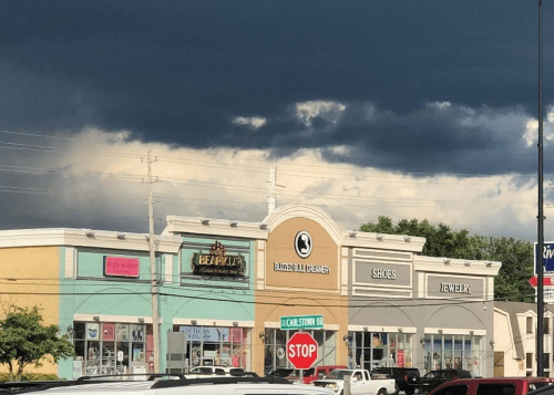A shopping plaza with various stores under a dark, cloudy sky, featuring a stop sign in the foreground.