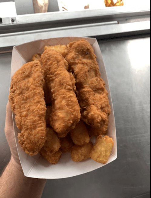 A hand holding a tray of crispy fried chicken tenders and golden tater tots.