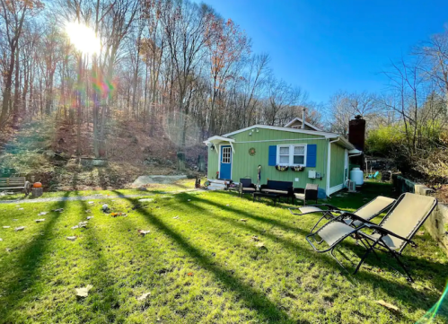 A green house surrounded by trees, with a sunny sky and long shadows on the grassy yard.