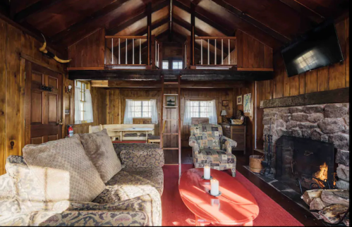 Cozy cabin interior with wooden walls, a stone fireplace, comfortable seating, and a warm, inviting atmosphere.