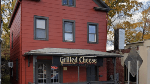 Red building with a sign reading "Grilled Cheese," surrounded by trees with autumn leaves.