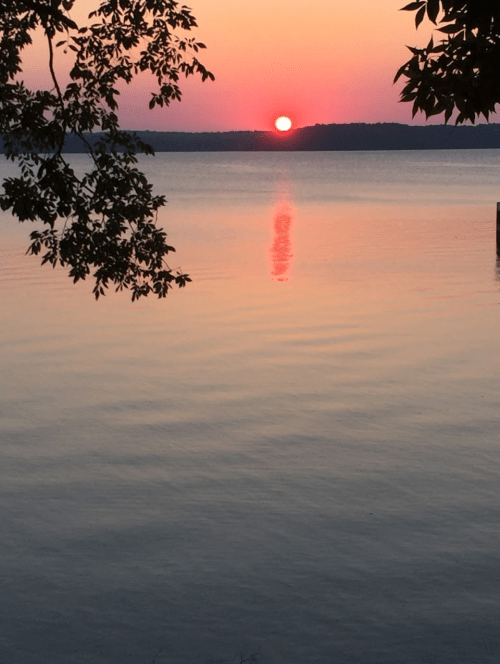 A serene sunset over a calm lake, with vibrant orange and pink hues reflecting on the water's surface.