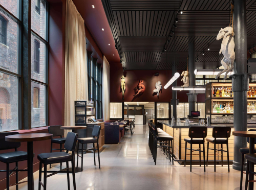 Modern restaurant interior featuring a bar, high tables, and artistic sculptures on the walls, with large windows.