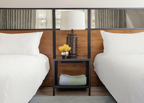 A cozy hotel room with two beds, a nightstand, a lamp, and decorative flowers between them.