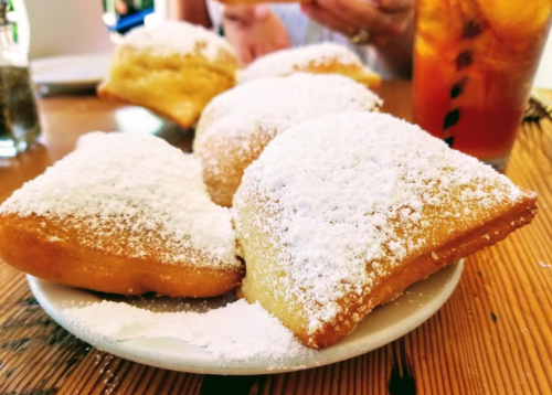 A plate of powdered sugar-dusted beignets, with a drink in the background.