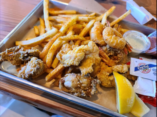 A tray of golden fries, fried shrimp, and crispy fried chicken, served with lemon and dipping sauces.