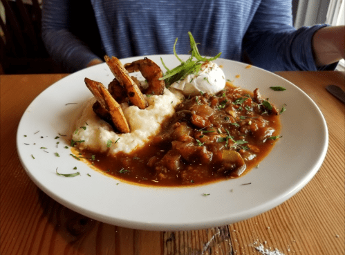 A plate of shrimp and grits topped with poached egg and garnished with green onions, served on a wooden table.