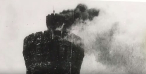 A black and white image of a tower emitting smoke from its top, surrounded by a hazy atmosphere.