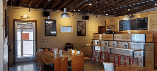 Cozy café interior with wooden tables, red stools, and a chalkboard menu on the wall. Bright and inviting atmosphere.