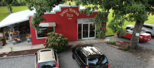 A red building with "Lookout Mountain Pizza" sign, surrounded by trees and parked cars in a gravel lot.