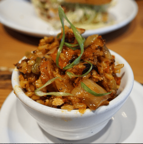 A small white bowl filled with spicy, sautéed vegetables and meat, garnished with green onions.