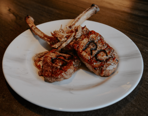 Grilled lamb chops on a white plate, garnished with onions and marked with the letters "PC."