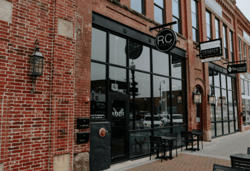 Exterior of a brick building featuring large glass windows and signage for "RC" and other businesses.