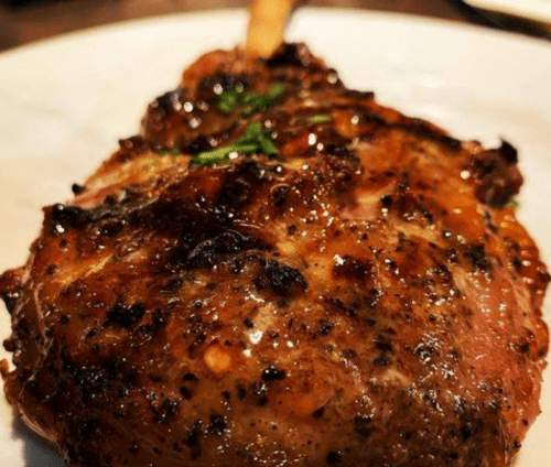 Close-up of a juicy, grilled meat chop garnished with herbs on a white plate.