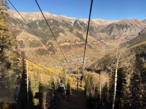 A scenic view from a gondola, overlooking a valley with autumn foliage and mountains in the background.