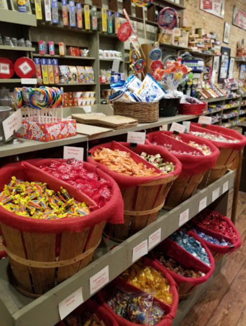 Colorful candy displayed in wooden baskets at a vintage store, with shelves of sweets and treats in the background.