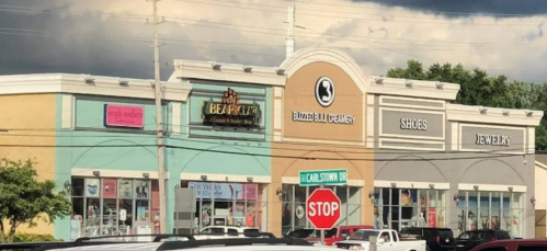 A shopping plaza featuring various stores, including a jewelry shop and a shoe store, under a cloudy sky.