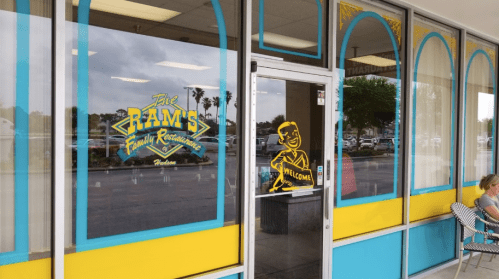 Exterior view of "The Ram's Family Restaurant" with colorful windows and a welcoming figure on the door.