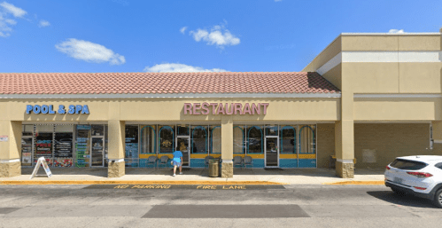 A restaurant storefront with colorful signage, next to a pool and spa shop, under a clear blue sky.