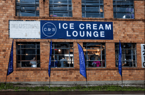 A brick building with a large sign reading "C&B Ice Cream Lounge" and blue flags outside, showcasing a cozy atmosphere.