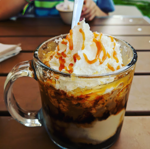 A glass cup filled with layers of dessert, topped with whipped cream and caramel drizzle.