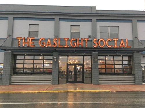 Exterior of The Gaslight Social, featuring a marquee sign with lights, on a rainy day.