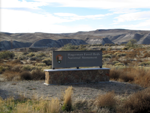 Sign for Hagerman Fossil Beds National Monument in a desert landscape with hills and sparse vegetation in the background.