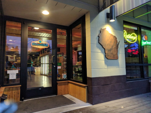 Entrance of a restaurant featuring a Wisconsin map sign, with warm lighting and a welcoming atmosphere.