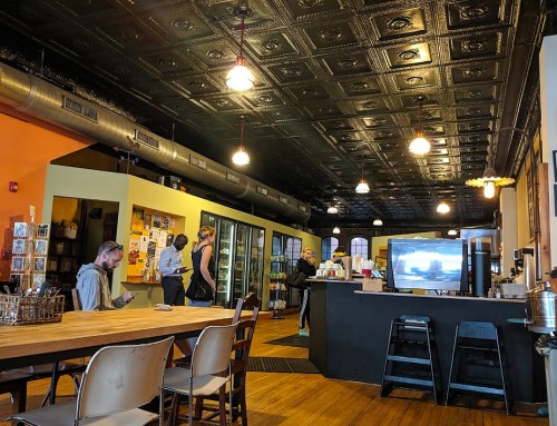 A cozy café interior with wooden tables, a counter, and patrons interacting, featuring a vintage ceiling and warm lighting.