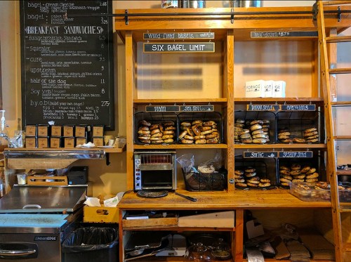 A cozy bagel shop display with shelves of bagels, a menu board, and a toaster oven.