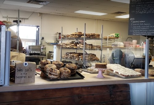 A bakery display with various baked goods, including cookies and bagels, behind a counter with a staff member working.