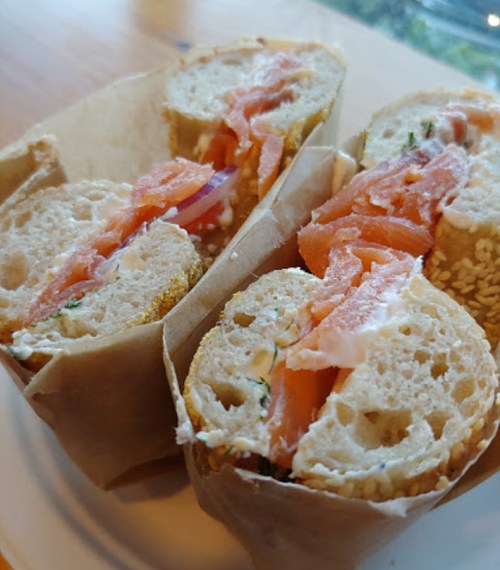 Two sesame bagels filled with cream cheese and slices of smoked salmon, wrapped in paper on a plate.