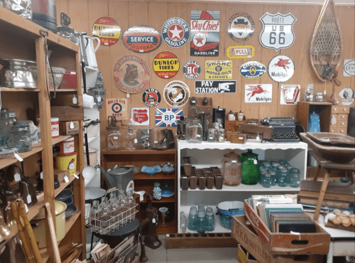 A vintage shop filled with various antique items, including signs, glassware, and a typewriter on display.
