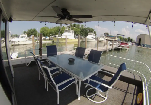 A covered patio with a glass table and chairs overlooking a marina with boats and a calm water view.