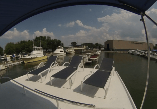 View from a boat deck with lounge chairs overlooking a marina filled with various boats and a cloudy sky.