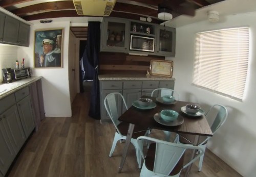 A cozy kitchen with gray cabinets, a wooden table set for four, and a nautical-themed painting on the wall.