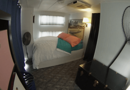 Cozy bedroom with a bed, colorful pillows, a fan, and a vintage trunk in a well-lit space.