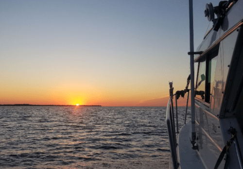 A boat is anchored on calm waters, with a vibrant sunset casting warm colors over the horizon.