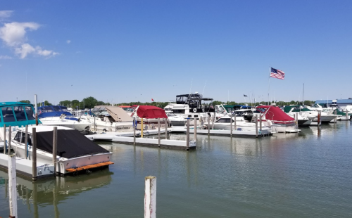 A marina with various boats docked, an American flag flying, and clear blue skies above.