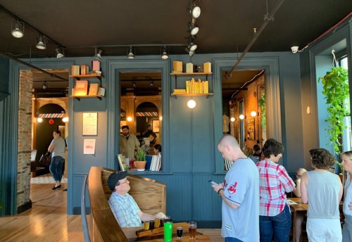 A cozy café interior with patrons seated, bookshelves, plants, and warm lighting creating a welcoming atmosphere.