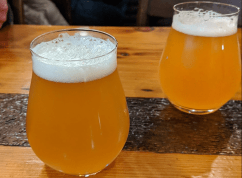 Two glasses of golden beer with frothy tops, sitting on a wooden table.