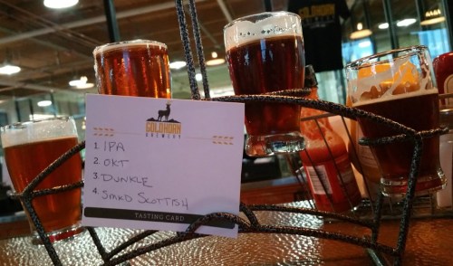 A tasting card with four beer samples: IPA, Oktoberfest, Dunkle, and Scottish, displayed on a metal holder.
