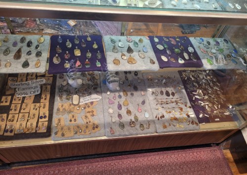 Display case filled with various gemstones and jewelry, including earrings and pendants, on purple and gray backgrounds.