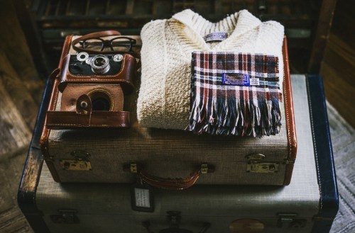 A vintage camera, a cozy sweater, and a plaid scarf arranged on an open suitcase.