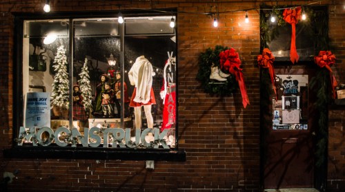 A festive storefront with holiday decorations, including wreaths and lights, showcasing vintage clothing and accessories.