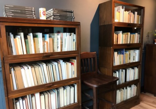 Two wooden bookshelves filled with books, with a wooden chair beside them against a dark wall.