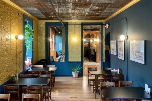Cozy restaurant interior with wooden tables, plants, and decorative walls in gold and blue tones.