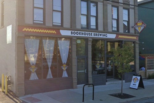Exterior of Bookhouse Brewing, featuring large windows, a sign, and decorative elements on a brick building.